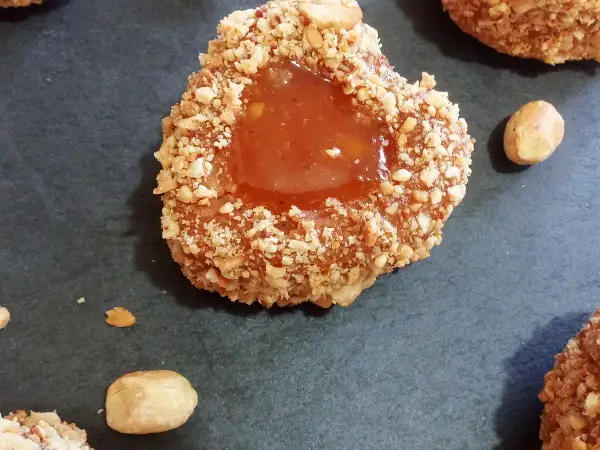 Un sablé algérien à la confiture, enrobé de noisettes concassées, sur fond sombre.
