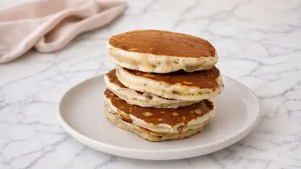 Pile de pancake banane moelleux sur une assiette, avec une serviette rose en arrière-plan.
