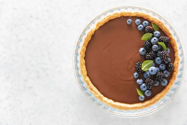 Une délicieuse tarte au chocolat au lait, garnie de myrtilles et de mûres fraîches, prête à être dégustée.