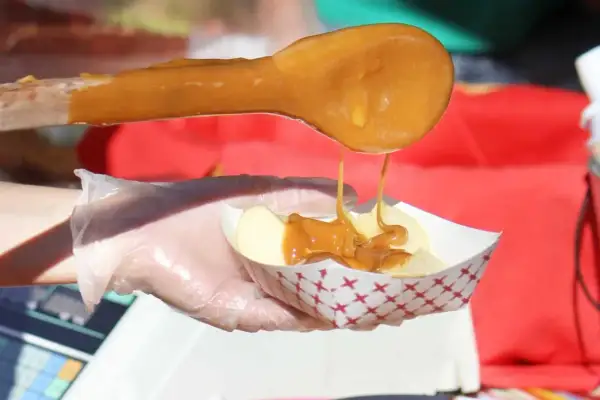 Une cuillère en bois verse du caramel coulant sur des tranches de pomme dans un petit bol. Le caramel est fait avec du sucre, quel sucre pour faire du caramel ?