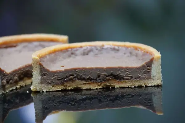 Tarte chocolat praliné croustillant, une tranche révèle sa texture onctueuse et sa base dorée.