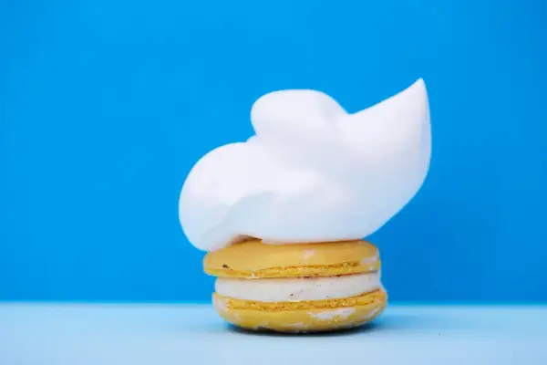 Un macaron jaune garni d'une crème blanche et surmonté d'une généreuse chantilly. Un délice qui rappelle la ganache chocolat macaron.
