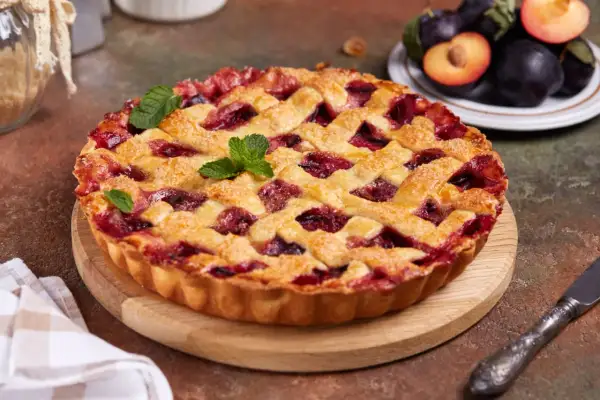 Tarte aux prunes maison, avec une croûte dorée et une garniture généreuse de fruits rouges, décorée de feuilles de menthe.