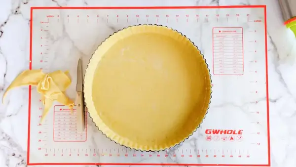 Préparation d'une conservation pâte brisée maison dans un moule à tarte, avec des chutes de pâte et un couteau.