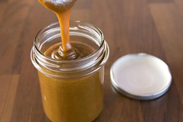 Caramel coulant versé dans un pot en verre, parfait pour une recette de pâte à tartiner noisettes maison.