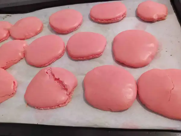 Coques de macarons roses sur une plaque de cuisson. Certaines sont parfaites, d'autres craquent, illustrant pourquoi les macarons craquent.