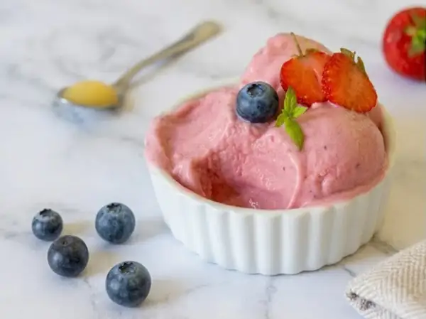 Délicieuse glace au yaourt maison aux fraises et myrtilles, garnie de fruits frais.