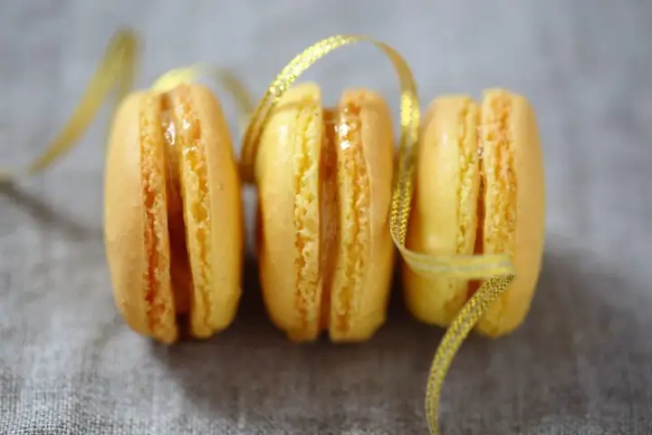 Trois macarons citron, parsemés d'un ruban doré scintillant. Une invitation à découvrir la recette macaron citron.