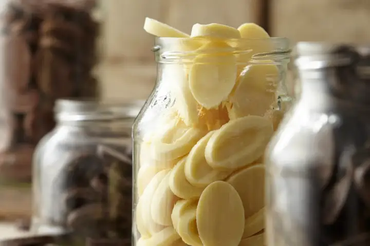Des éclats de chocolat blanc dans un bocal, prêts pour la conservation chocolat maison. Des fèves de cacao dans d'autres bocaux en arrière-plan.